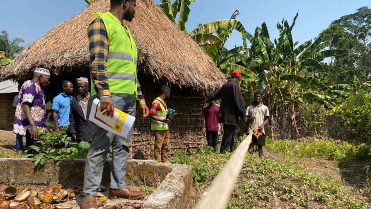 A group of people, one in a yellow construction vest, and a young person using a measuring tape in the soil.