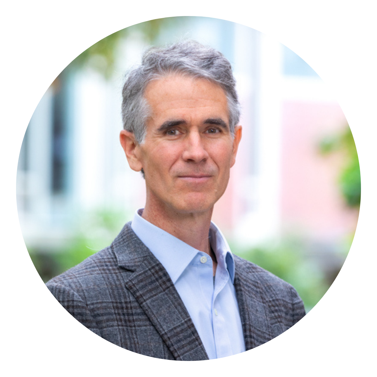 a man in a grey plaid sport coat with grey hair with a bokah outdoor background