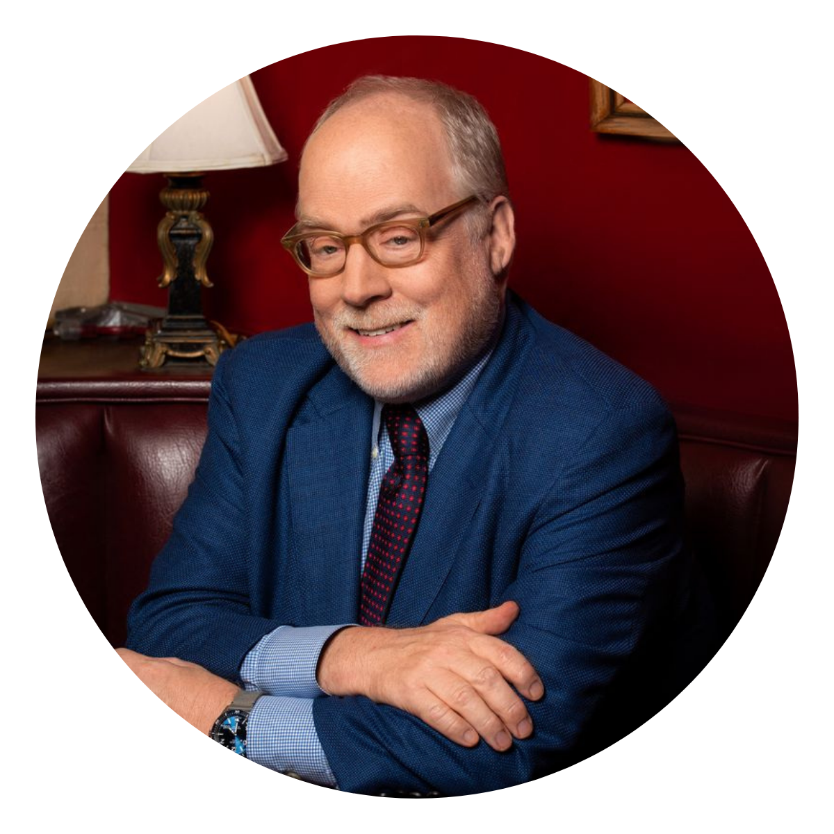 A man with a blue suit and burgundy tie in front of a red all