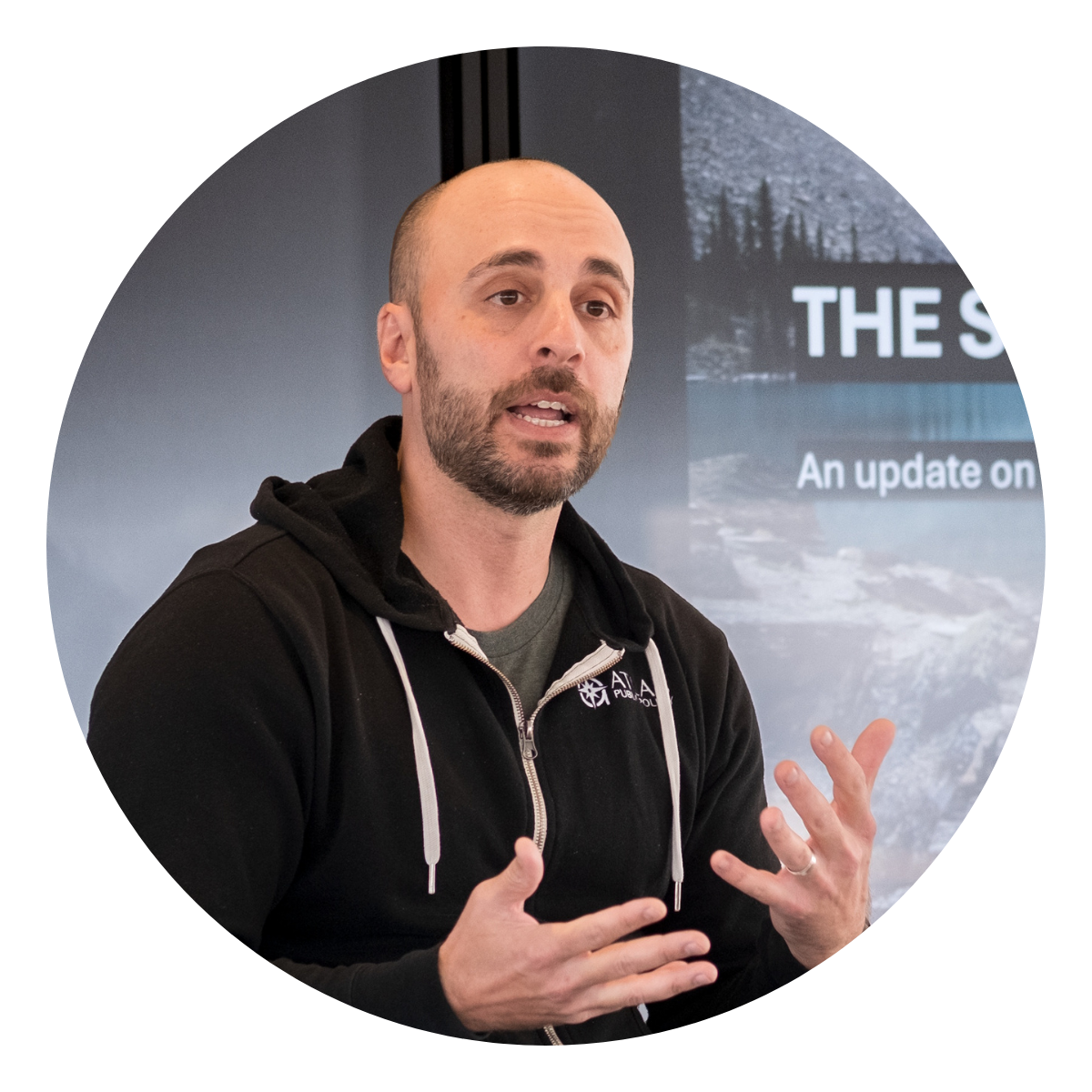 a man in a black hoodie talking and gesturing with his hands