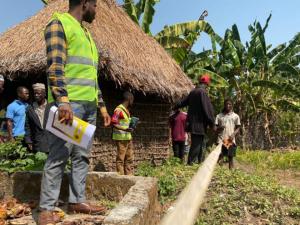 A group of people, one in a yellow construction vest, and a young person using a measuring tape in the soil.