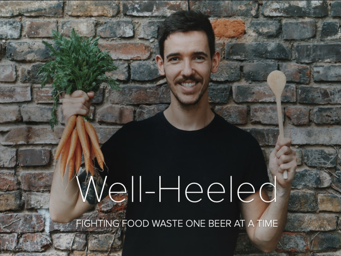 Daniel Anthes holding a bunch of carrots and a wooden spoon in front of a stone wall. The title reads "Well-Heeled: Fighting food waste one beer at a time""