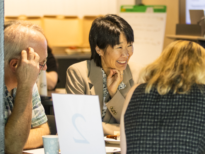 A professor with short dark hair and a beige blazer smiles across the table 