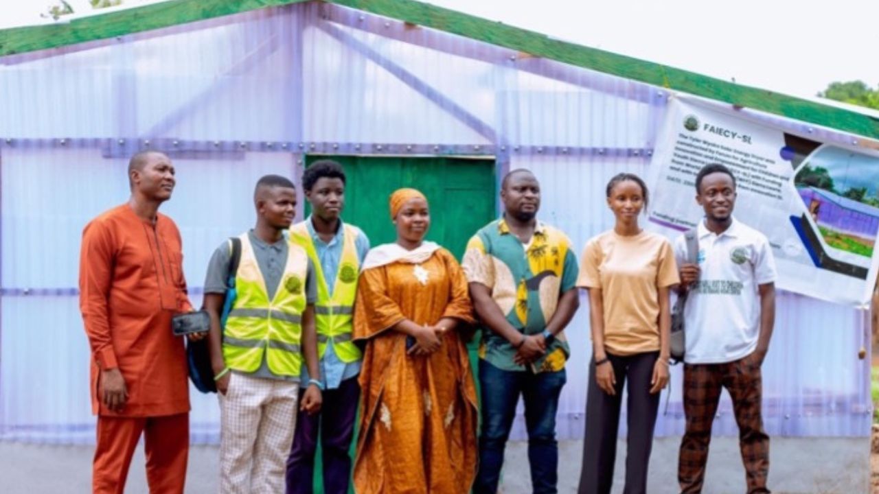 Seven people standing outside in front of the solar dryer.