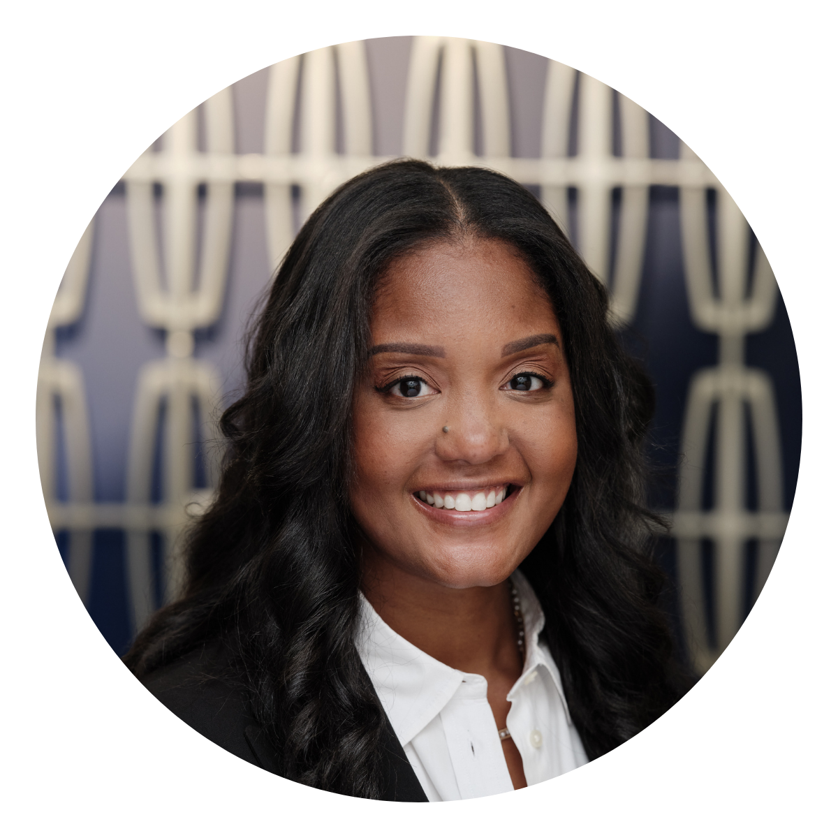 Deanne Millison a woman with dark long hair and a black blazer in front of a patterned wall