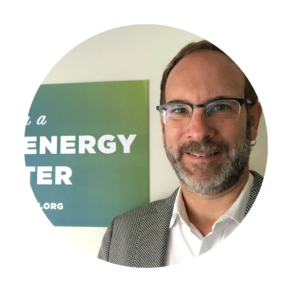 Jeremy Pittman a man with glasses and a grey blazer standing in front of a green sign on a wall