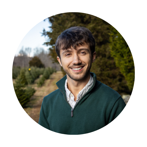 Max Sano a man in a green three-quarter zip with dark brown hair in front of outdoor scene with trees