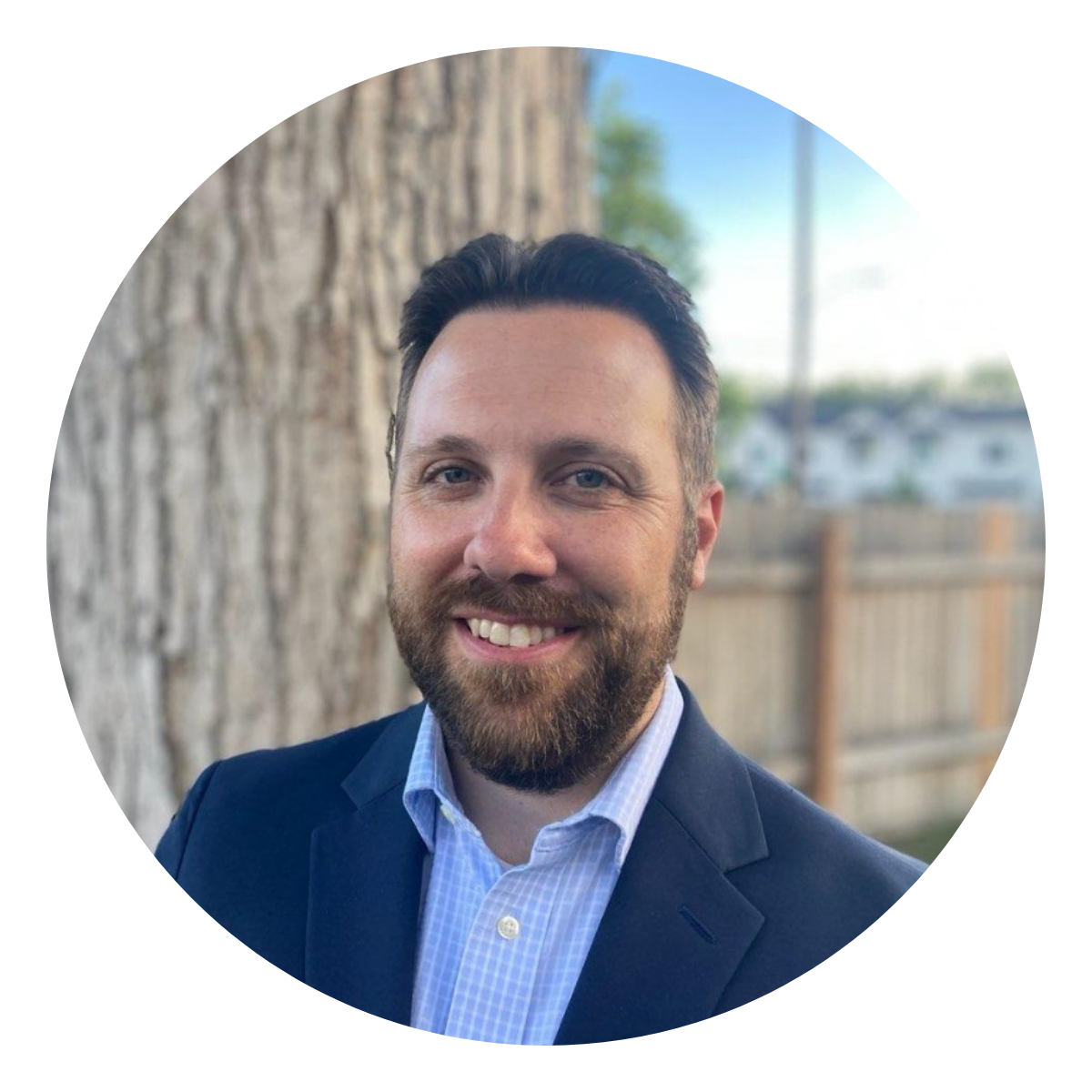 Michael King a man with brown hair and a beard in a navy sport coat standing in front of a tree trunk