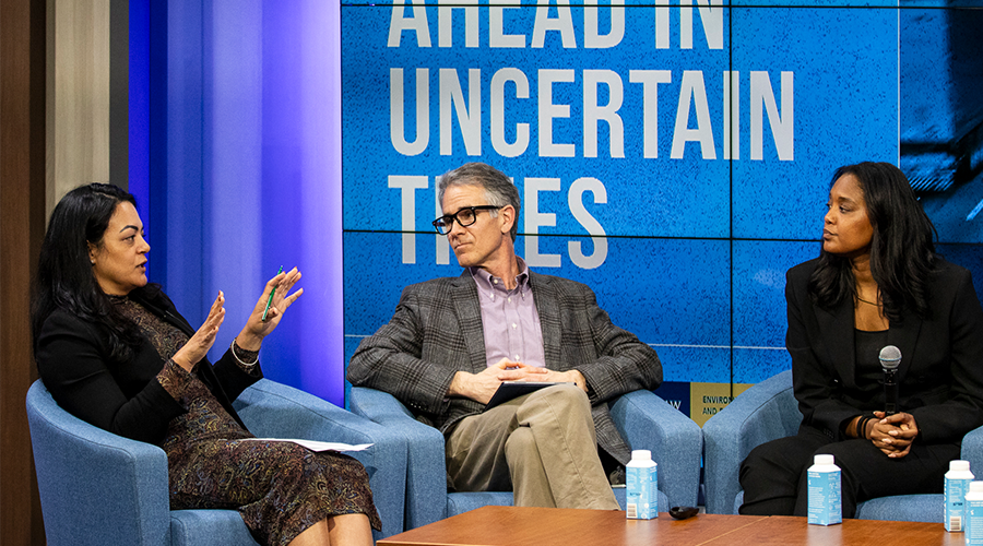 three people sit talking in blue chairs on a stage against a blue backdrop