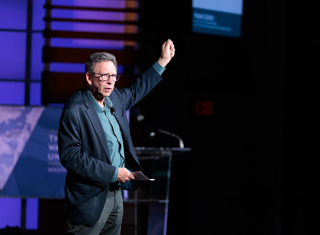 Frank Sesno raises is arm in a call to action on stage