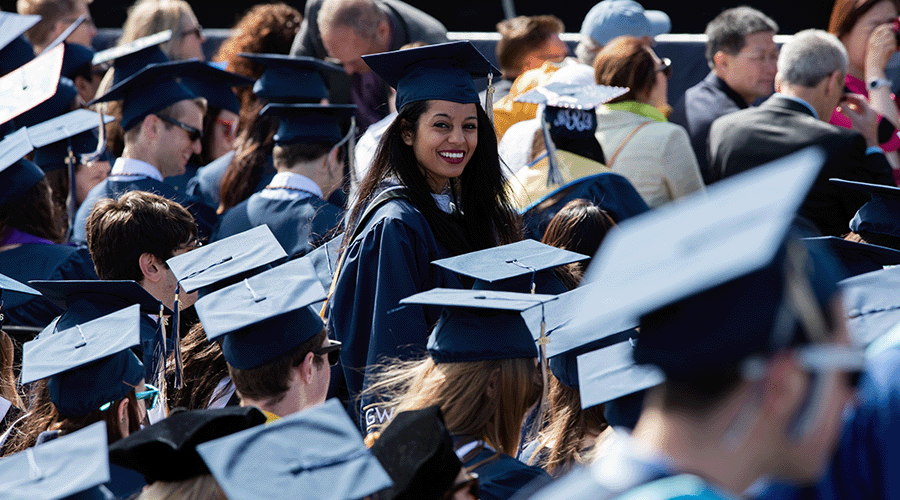 a GW graduate smiles at the camera in the middle of commencement