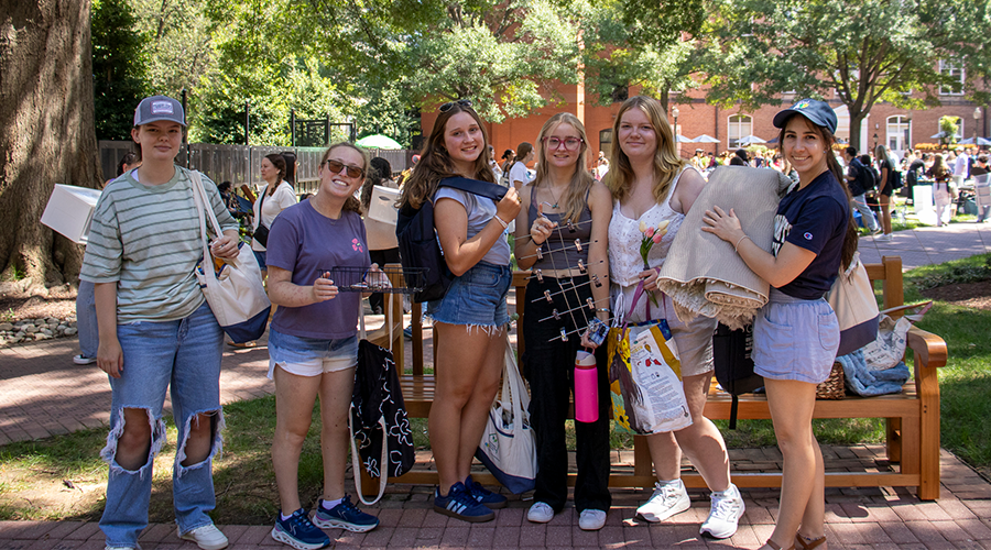 LLC Academics A group of six people stand in the middle of a college campus holding stuff at a yard sale