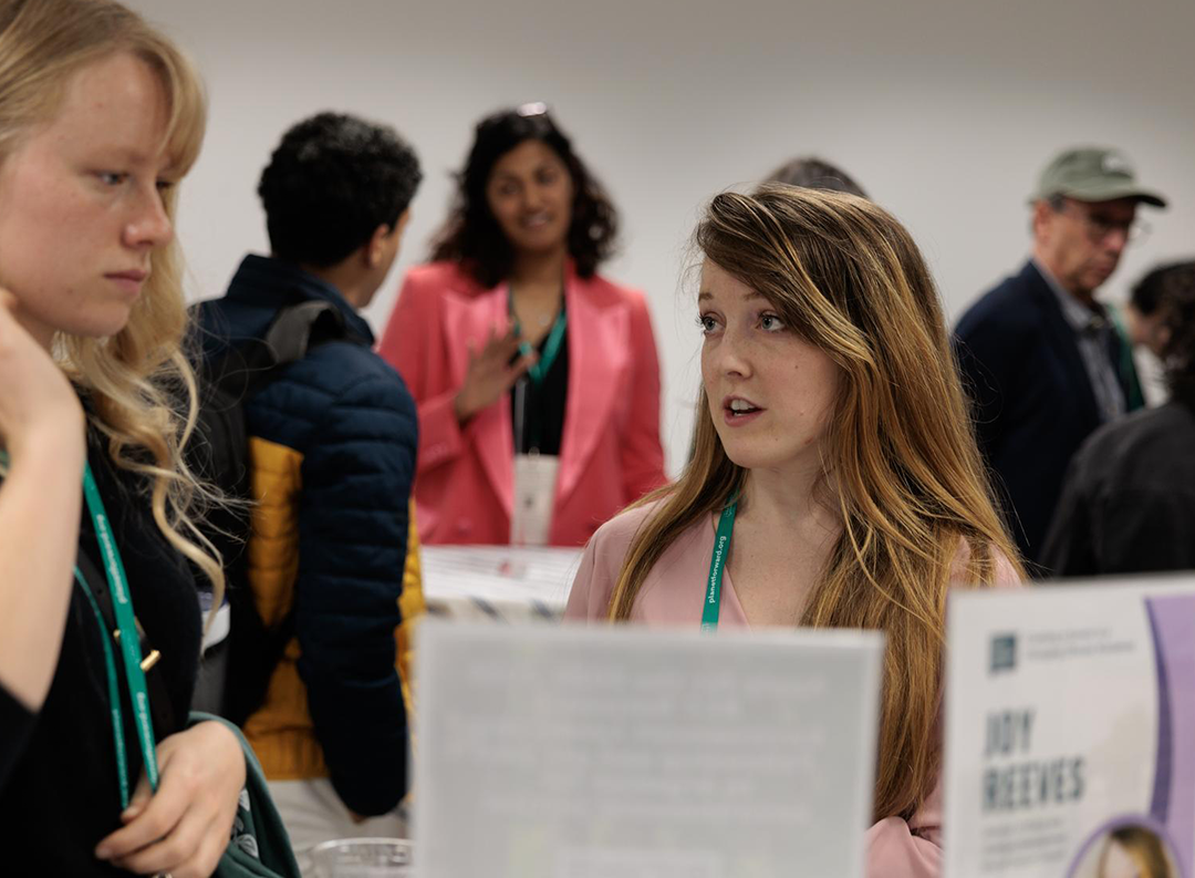 Networks LLC a person with long light hair speaks to a student with a green lanyard
