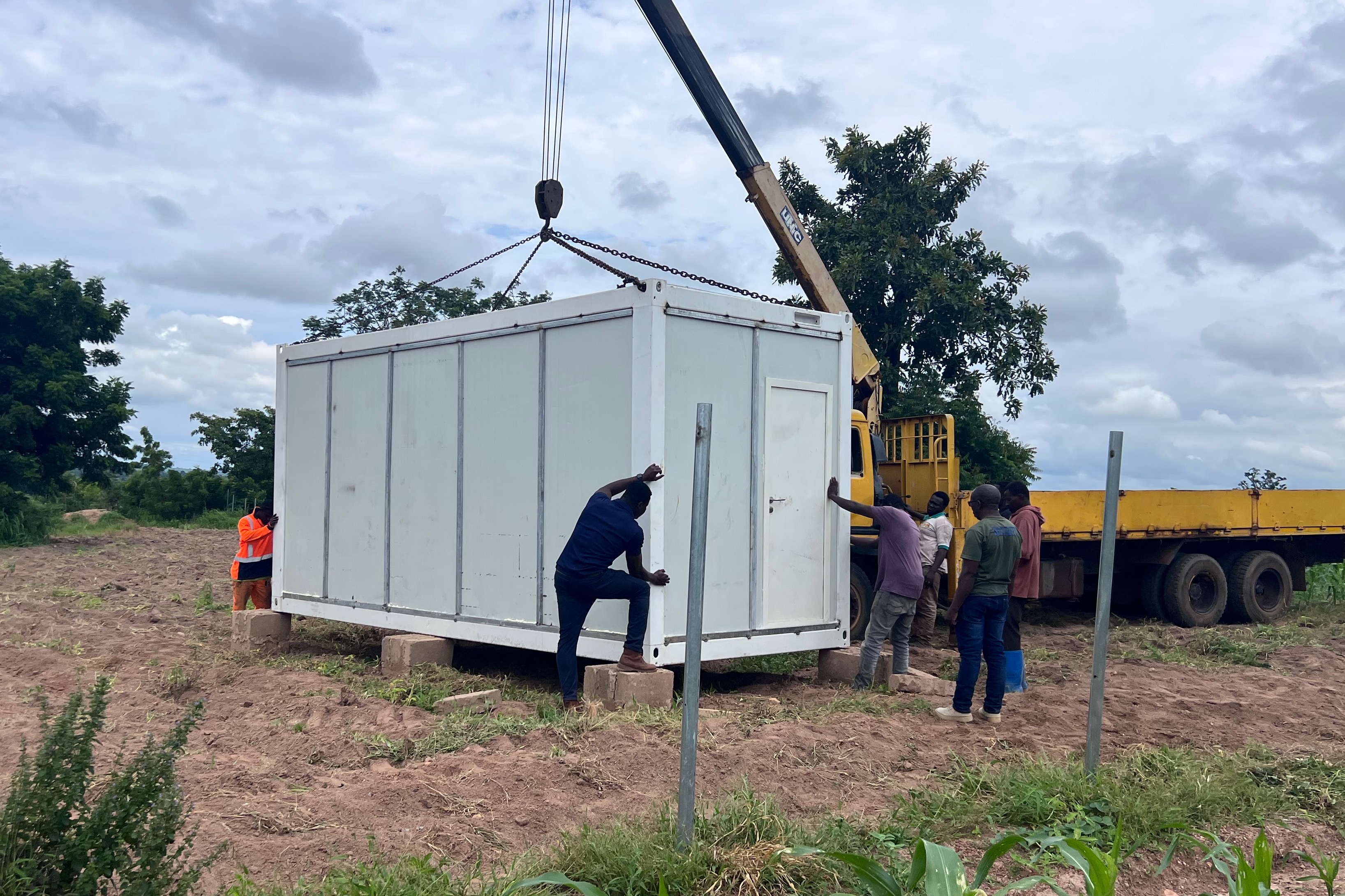 a group of three people around a crane holding a white large container box