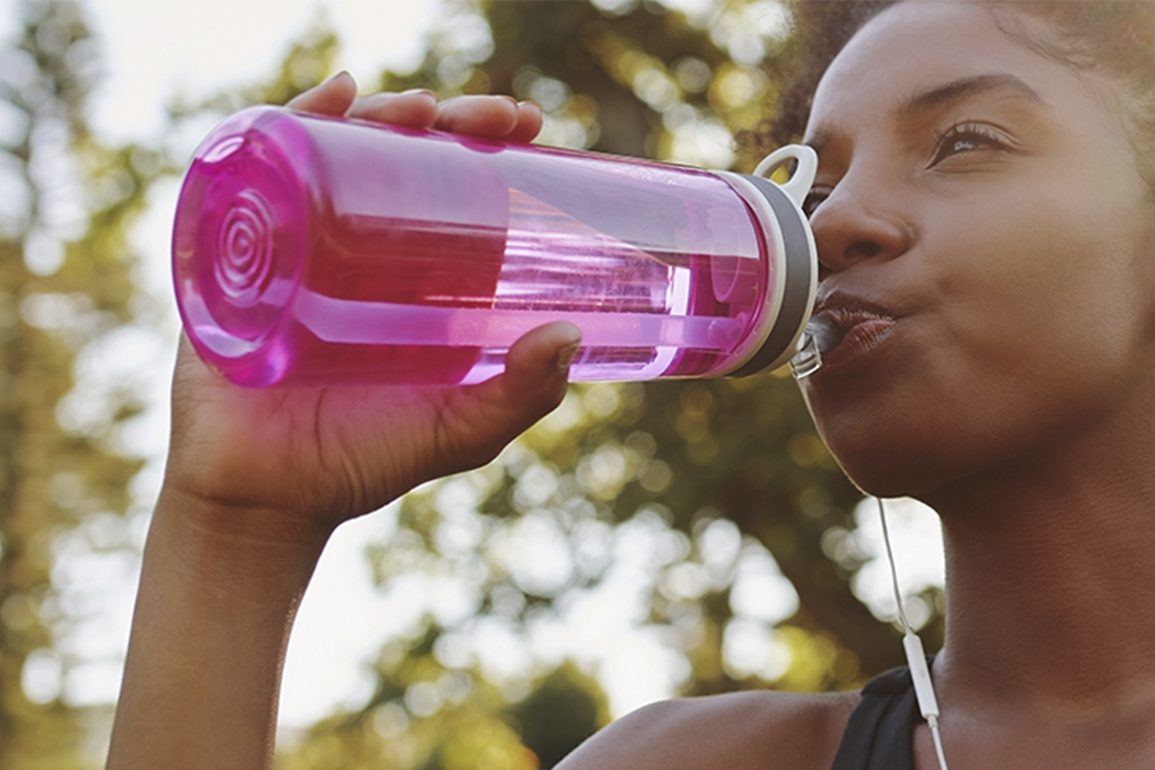 a woman with a pink water bottle drinks outside