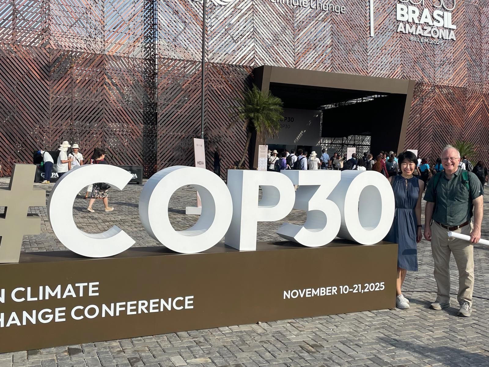 a big white sign that reads COP30 and two people standing to the right