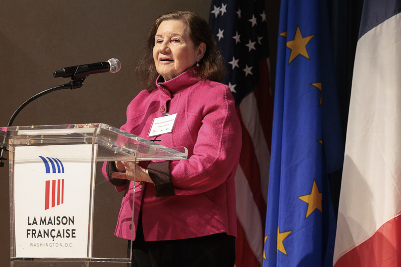 a woman in a pink sport coat speaks at a podium