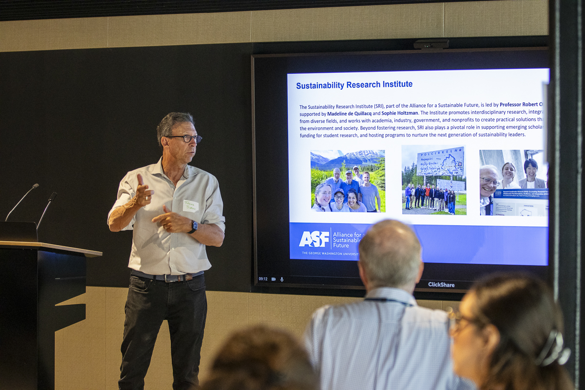 a man in a white shirt stands in front of a screen speaking
