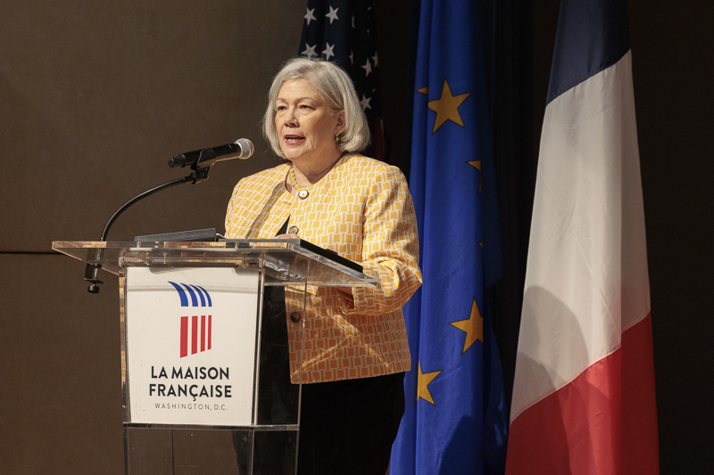 a person in a yellow vest speaks at a podium in front of a French flag