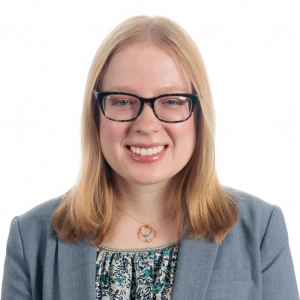 Erin Carlin smiling, wearing glasses, a gold necklace, and a blue blazer with blouse