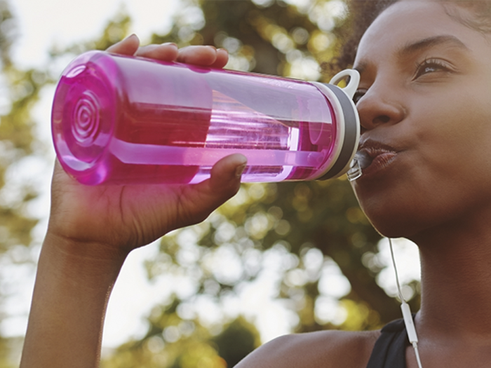 a woman with a pink water bottle drinks outside
