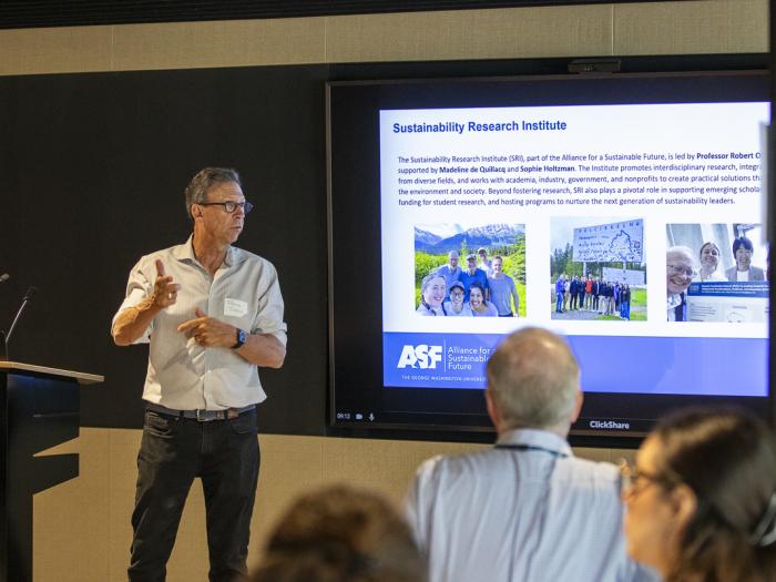 a man in a white shirt stands in front of a screen speaking