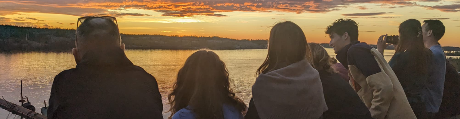 a group of eight students looking over a body of water at sunset