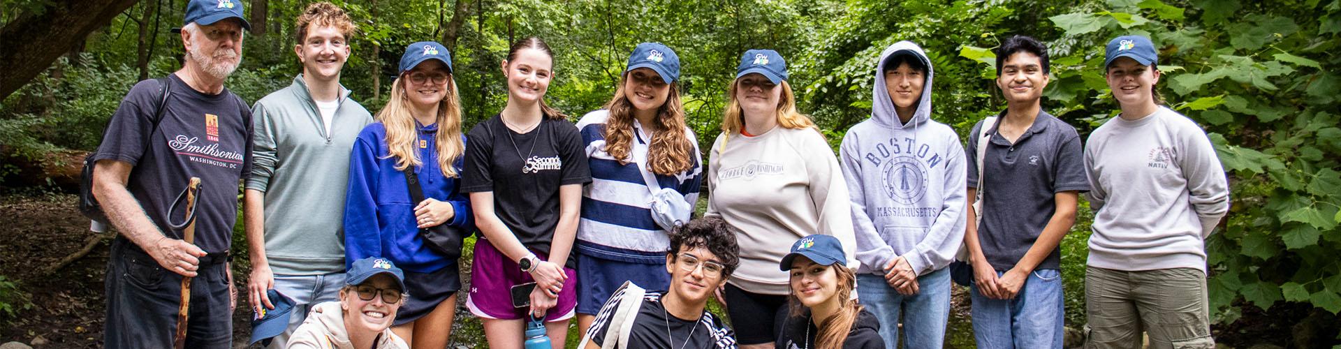 A group of 12 students and a professor stand in a forest 
